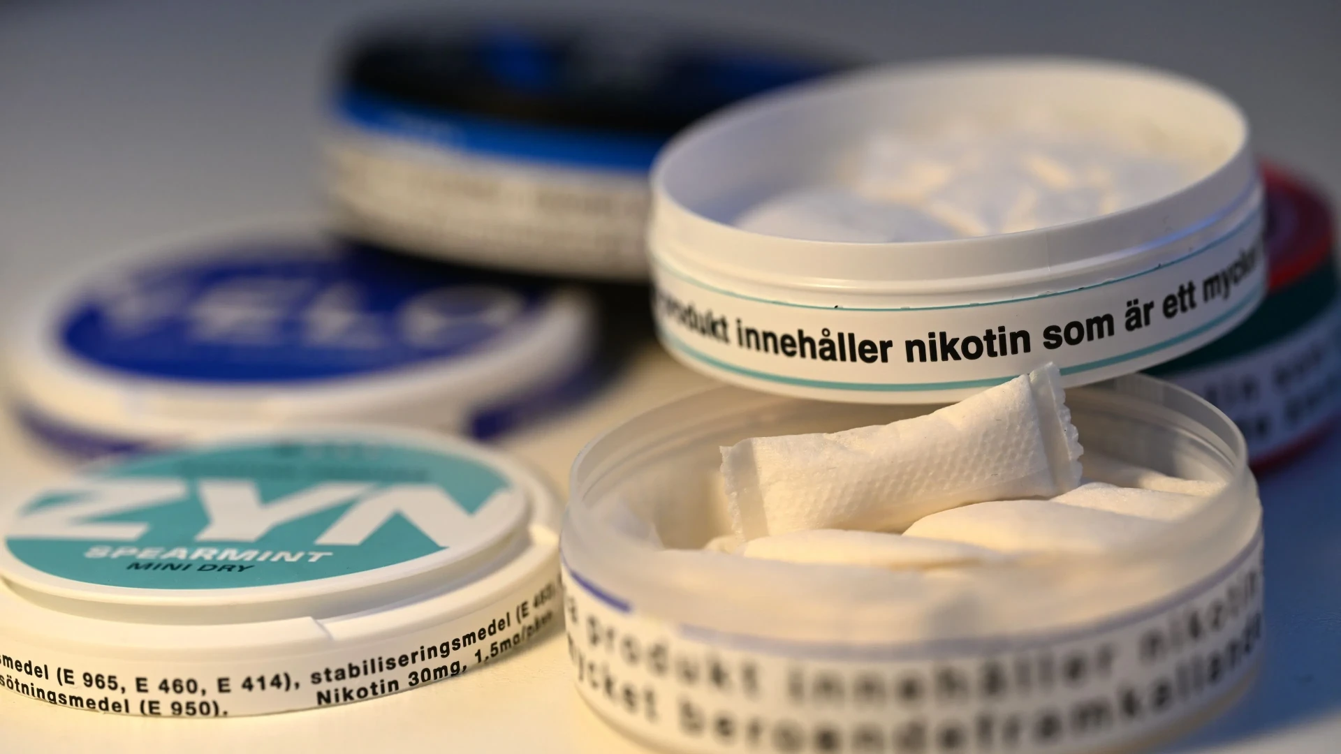 Três latas de snus alinhadas em fundo bege representando diferentes forças de nicotina