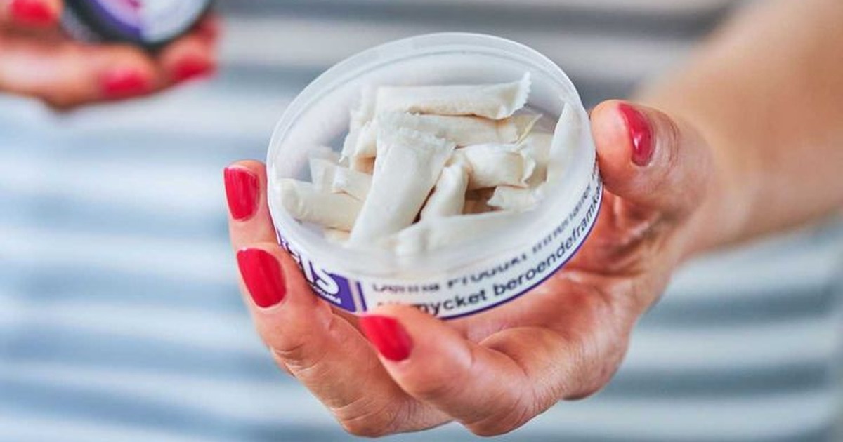 Lata branca de snus ao lado de um relógio analógico em fundo bege